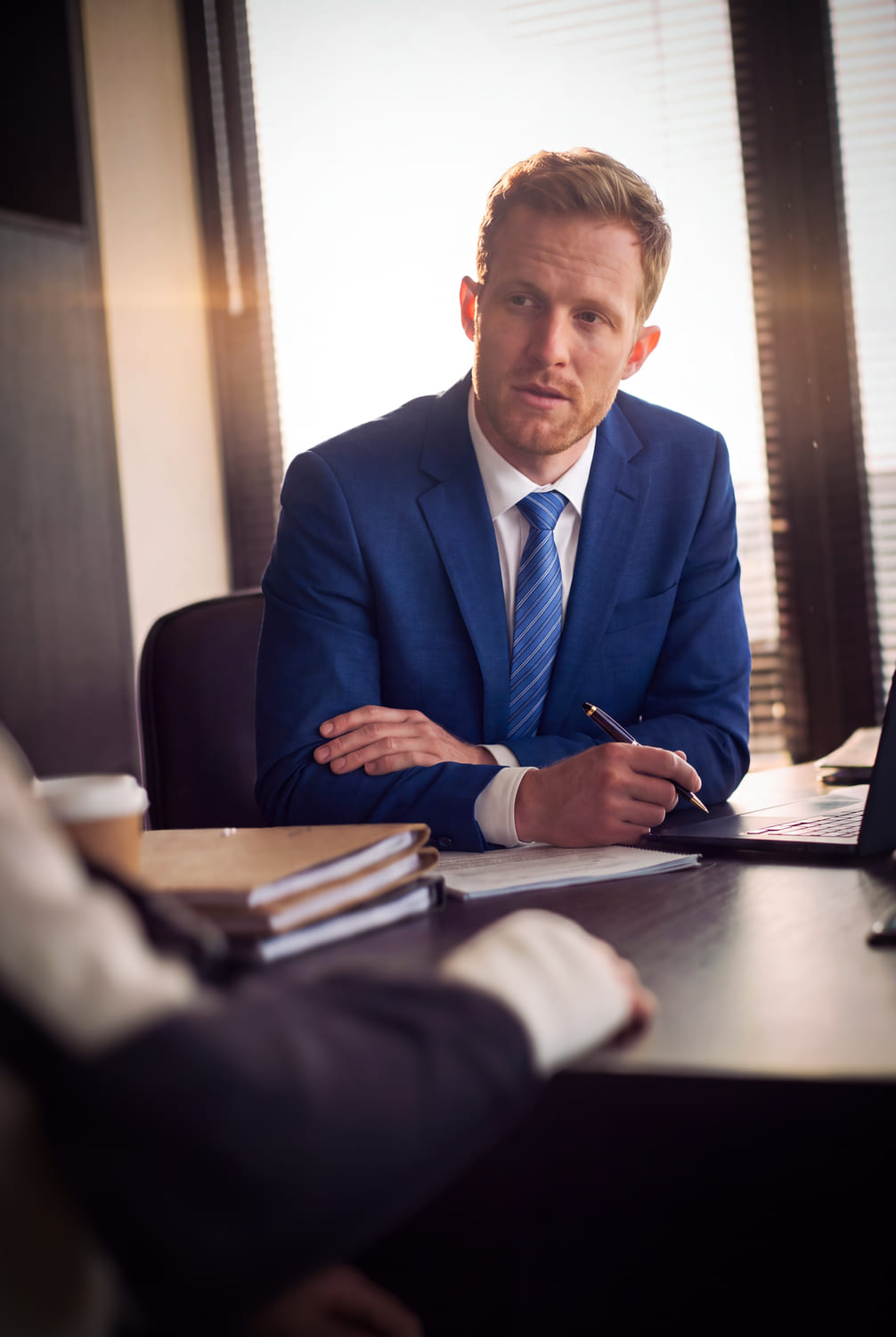 An attorney at his desk, pen in hand, case files and a laptop in front of him.